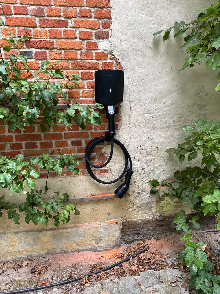 Zwarte Easee-lader met laadkabel aan een tuinmuur tussen het groen, geplaatst door Laadnatie.