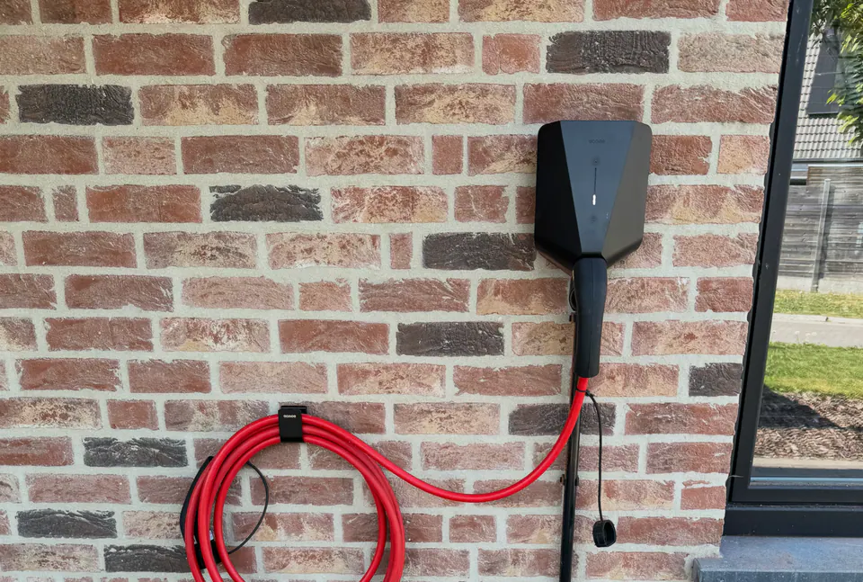 Zwarte Easee-lader met rode laadkabel aan een bakstenen muur, geplaatst door Laadnatie.