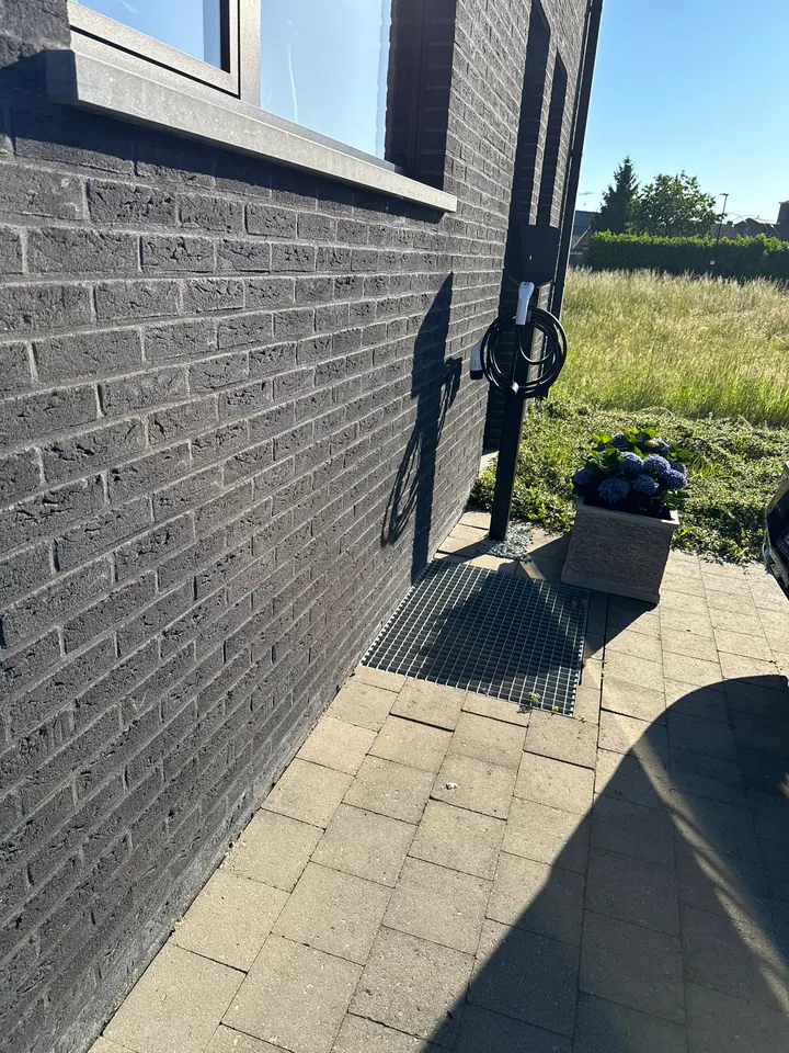 Witte lader op een zwarte montagepaal naast een donkere gevel, geplaatst door Laadnatie.
