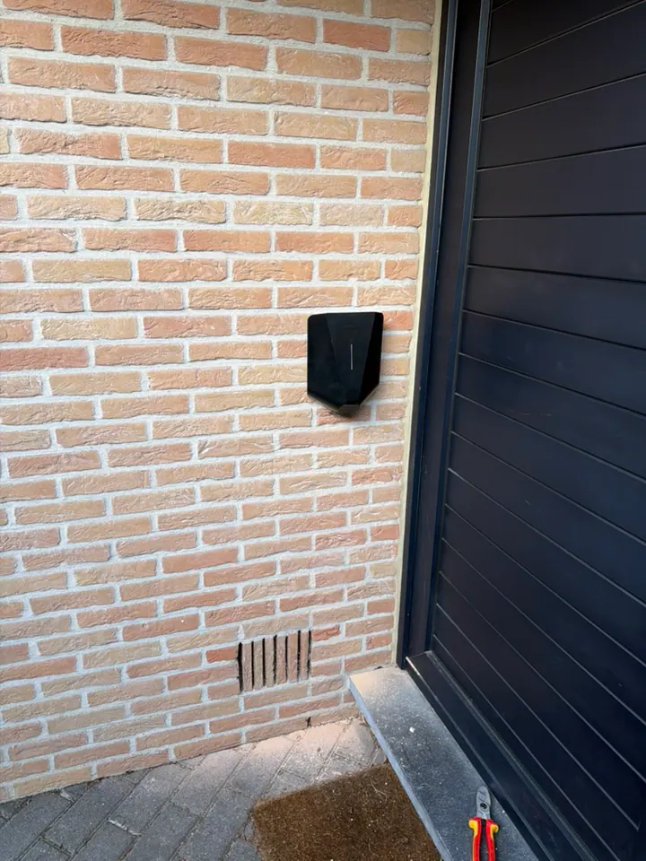 Zwarte Easee-lader aan een bakstenen muur naast de garagepoort, geplaatst door Laadnatie.