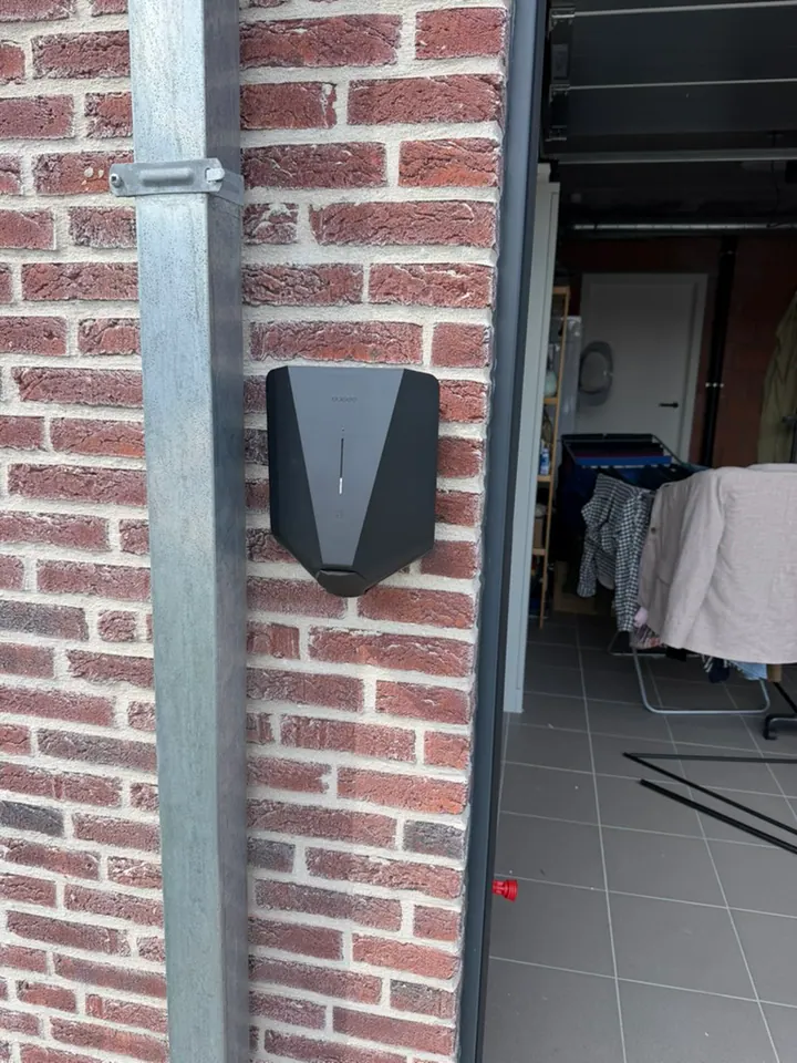 Zwarte Easee-lader aan een bakstenen garagemuur, geplaatst door Laadnatie.