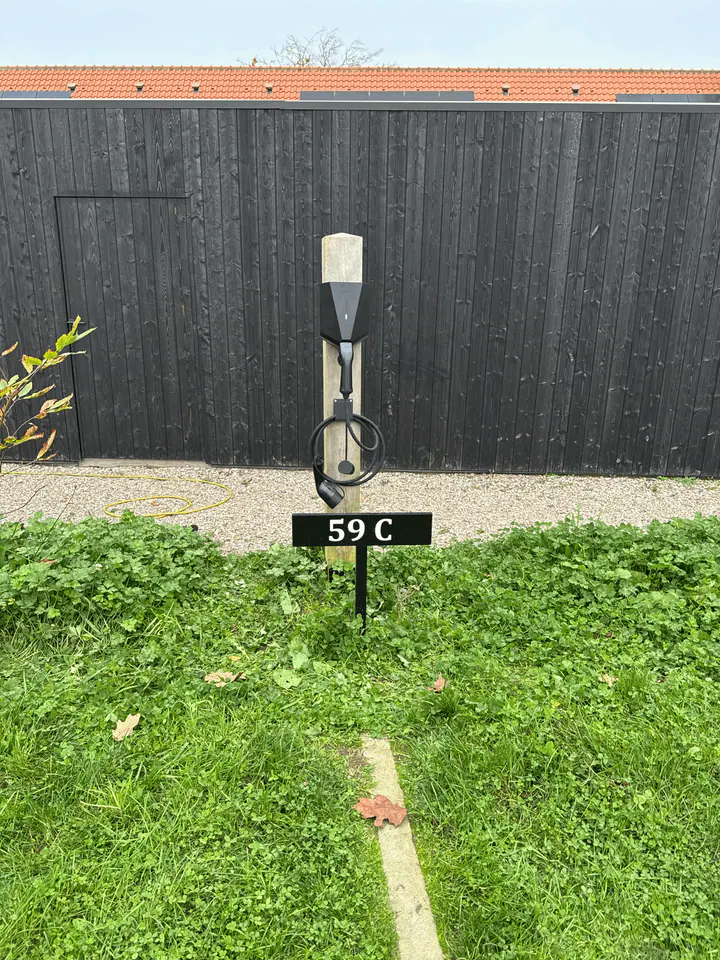 Zwarte Easee-lader op een houten montagepaal voor een zwarte schutting, geplaatst door Laadnatie.