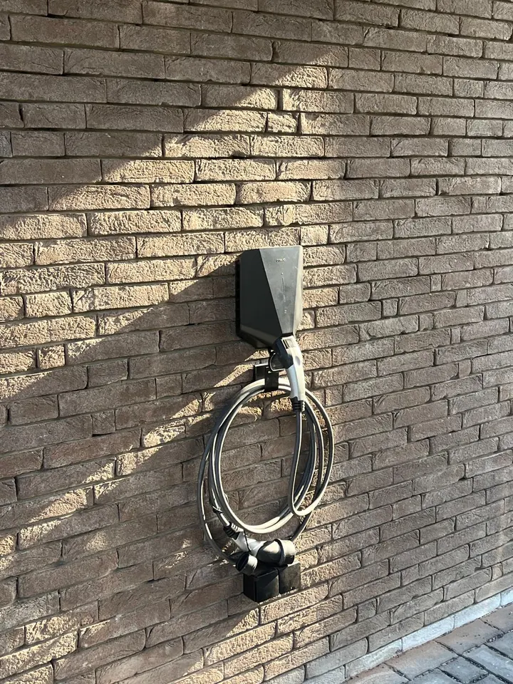 Zwarte Easee-lader met opgerolde laadkabel aan een donkere bakstenen muur, geplaatst door Laadnatie.