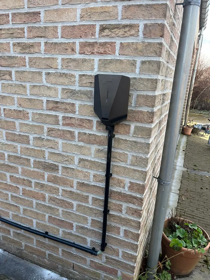 Zwarte Easee-lader met laadkabel aan de hoek van een lichtbruine bakstenen gevel, geplaatst door Laadnatie.
