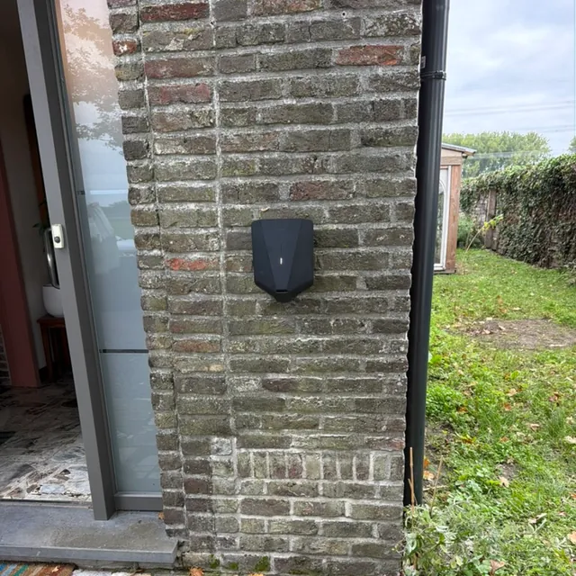 Zwarte Easee-lader aan een bakstenen buitenmuur naast een glazen tuindeur, geplaatst door Laadnatie.